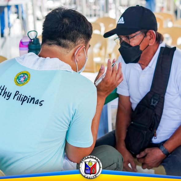 Litrato: lalaking nakikipag-usap sa telepono habang may kasamang nakikinig sa Naic Town Plaza flu vaccine caravan