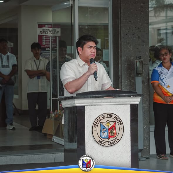 Isang opisyal na nagsasalita sa podium habang nakikinig ang mga kawani sa harap ng Municipal Hall ng Naic
