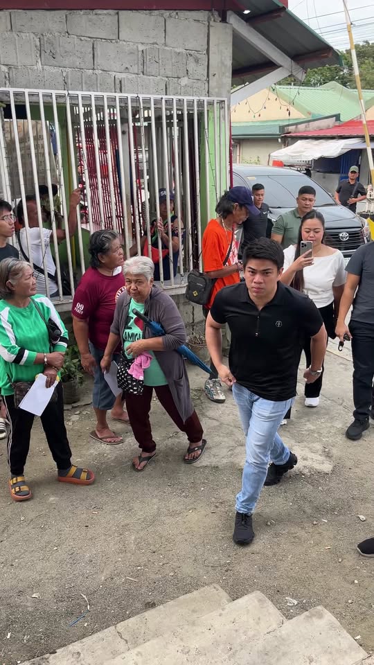 Mga tao sa labas ng gate habang naglalakad ang isang lalaki sa Villa de Adelaida Homes, Barangay Halang