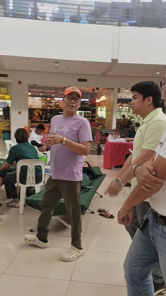 Mga tao sa mall concourse habang may nagsasalita sa Blood Donation Drive sa Stadium Shopping Strip