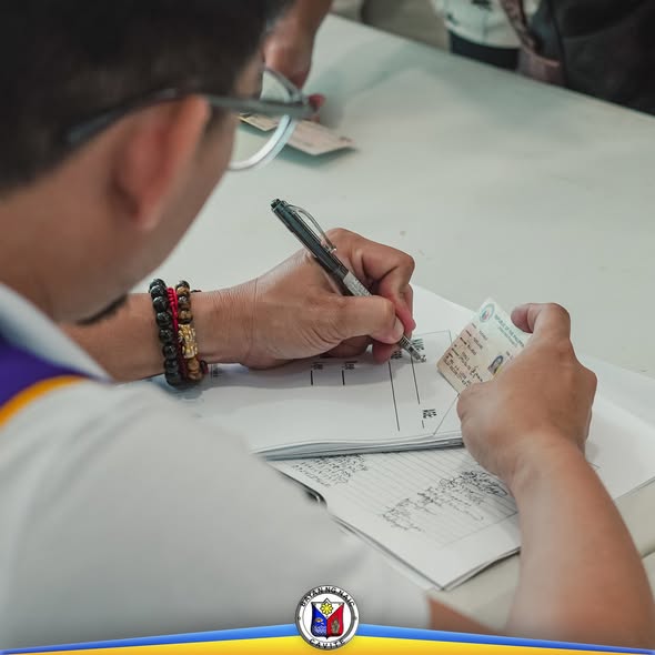 Taong nagsusulat sa papel habang hawak ang card sa libreng eye check-up at screening sa Sabang, Naic