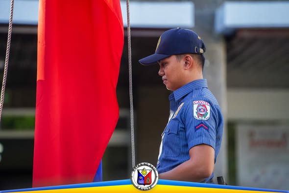 Lalaking nakauniporme habang nakatayo nang tuwid sa tabi ng watawat sa Flag Raising Ceremony sa Naic Municipal Hall