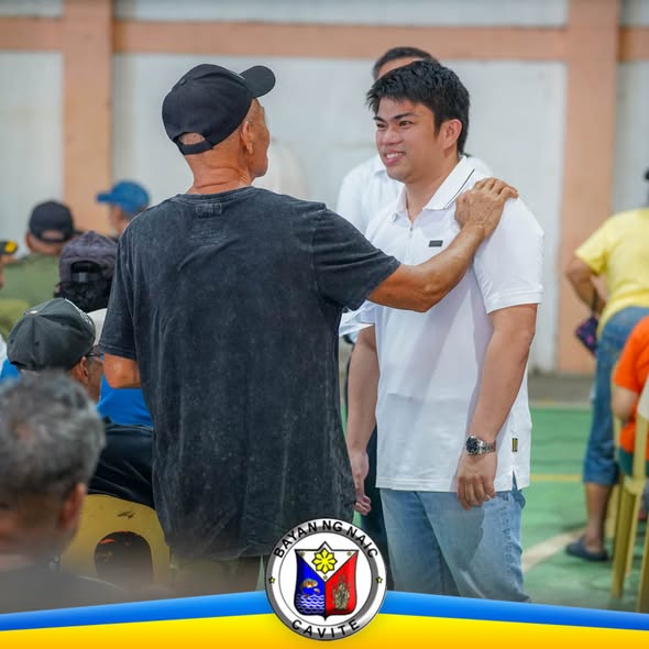 Lalaking naka-puting polo na nakangiti habang kausap ang isang senior citizen sa loob ng covered court