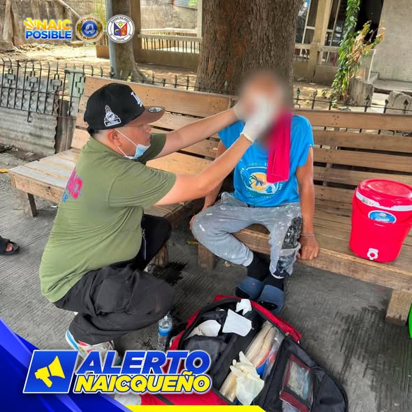 Rumespondeng MDRRMO na tumutulong sa pasyenteng nakaupo sa bench sa Brgy. Ibayo Silangan, Naic