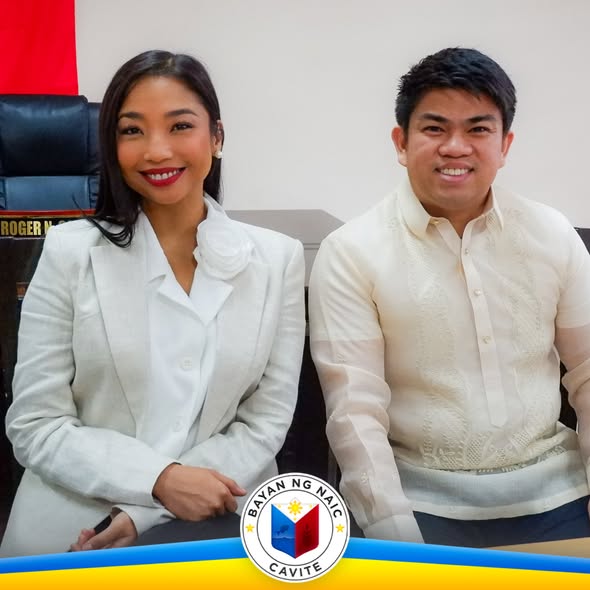 Dalawang taong nakangiti sa harap ng upuan sa opisina, may logo ng Bayan ng Naic Cavite sa ibaba