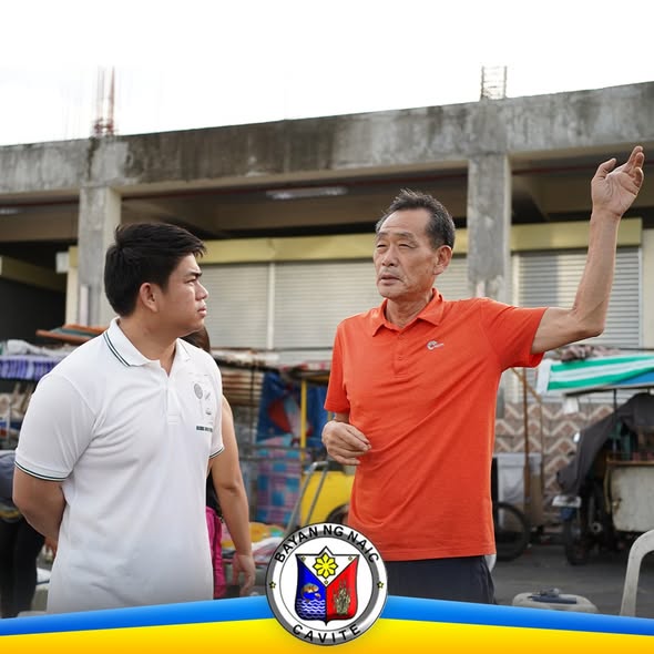 Litrato: Nakikipag-usap ang isang lalaki sa isang kasama habang nakataas ang kamay sa palengke ng Naic