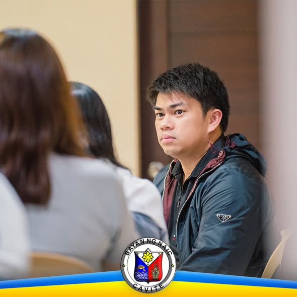 Lalaking nakaupo sa pulong sa loob ng silid, may dalawang taong nasa harapan