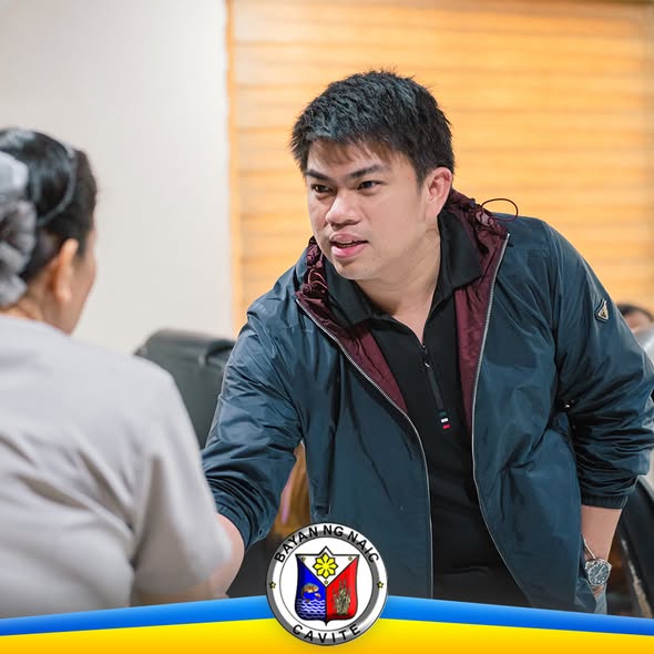 Isang opisyal na nakikipag-usap sa isang babae sa loob ng opisina, may logo ng Bayan ng Naic