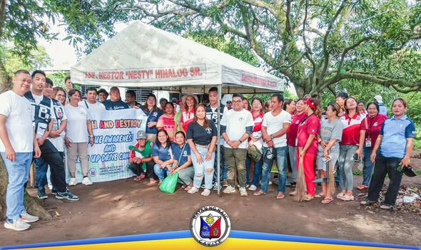 Grupo ng mga volunteer at opisyal na nagkakaisa sa Search and Destroy Dengue Awareness sa ilalim ng tent sa Naic