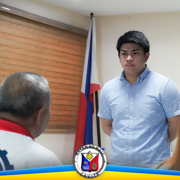 Pulong sa opisina ng Naic habang nag-uusap ang dalawang lalaki sa harap ng watawat ng Pilipinas
