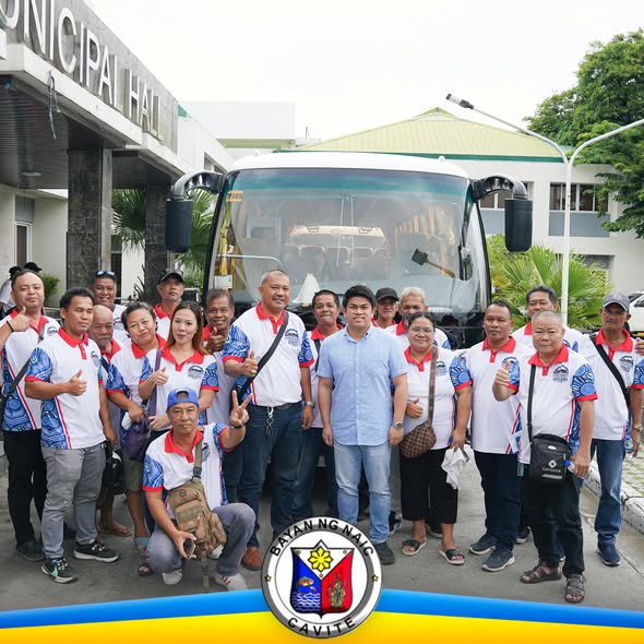 Grupo ng mga tao sa harap ng modernong bus at Municipal Hall ng Naic, nagpapose habang nagpapakita ng thumbs up
