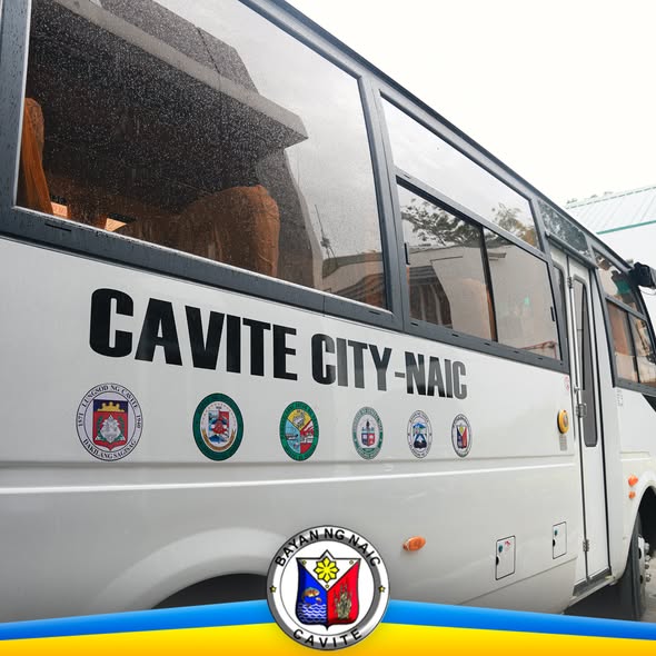 Puting bus na may nakasulat na "Cavite City-Naic" at mga emblem sa gilid, nakaparada sa labas