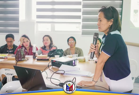 Babaeng nagsasalita sa mikropono habang nakikinig ang mga dumalo sa Mandatory Training para sa mga kooperatiba