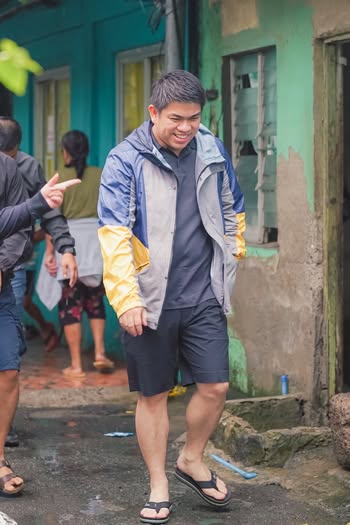 Litrato: Lalaking nakangiti habang naglalakad sa makitid na eskinita sa gilid ng mga bahay, sa ocular inspection ng Naic
