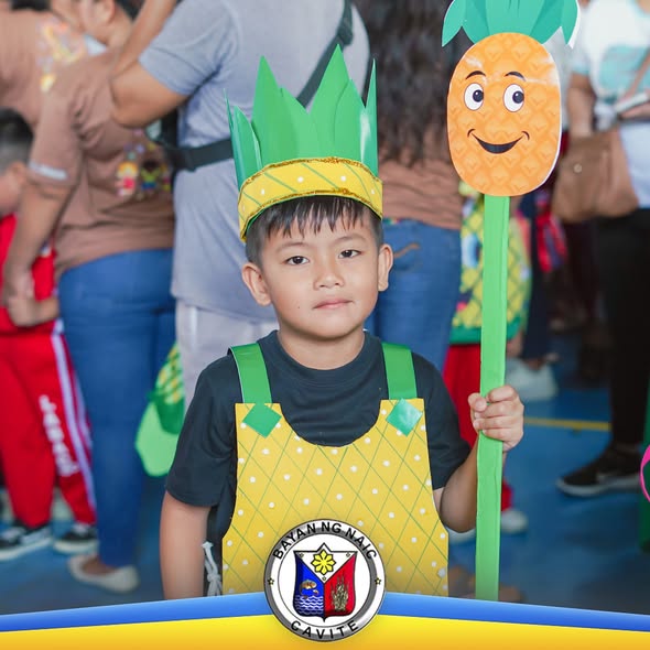 Batang nakasuot ng costume na pinya habang may hawak na malaking cutout ng pinya sa Nutrition Month celebration