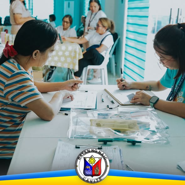 Mga kababaihan na nagsusulat ng forms sa mesa habang may mga staff sa likuran sa Family Planning Caravan sa Naic