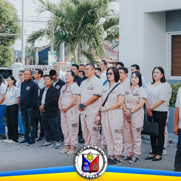 Mga kawani at opisyal na nakatayo nang maayos sa harap ng gusali habang nagaganap ang flag raising ceremony sa Naic