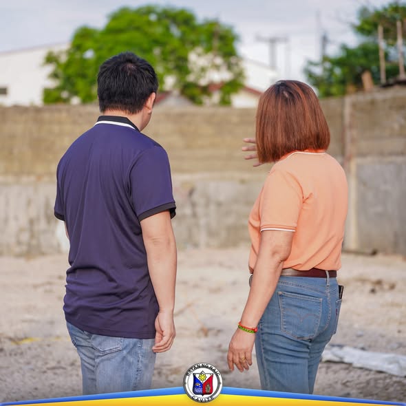 Dalawang tao na nakatalikod habang tinitingnan ang lugar na may pader sa Naic Public Market