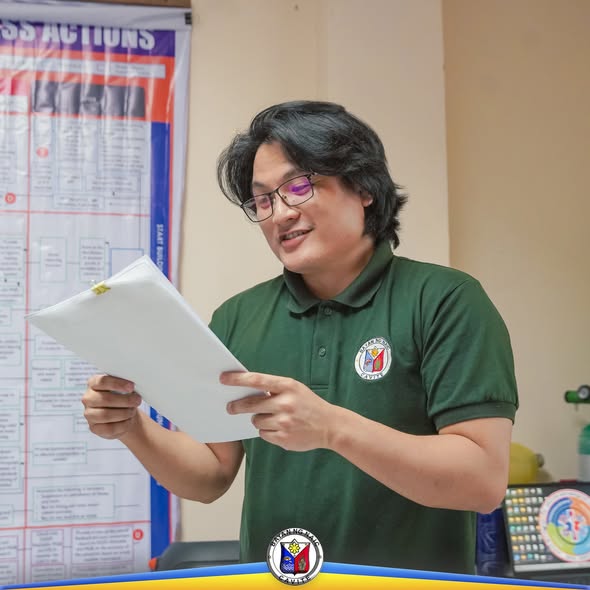 Lalaking nagbabasa ng papel sa opisina habang may chart sa likod, bahagi ng Basic Life Support training ng Naic RHU