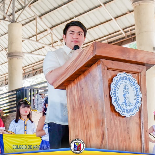 Lalaki na nagsasalita sa podium sa covered court habang may mga batang estudyante sa likod sa Sports Festival