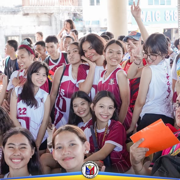 Grupo ng mga estudyanteng nakasuot ng maroon at puting jersey, nakangiti habang nagpapakuha ng larawan sa Naic Sports…