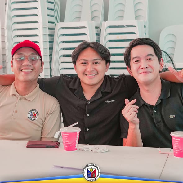 Tatlong kabataang lalaki na nakangiti habang nakaupo sa mesa na may pink na baso ng inumin.