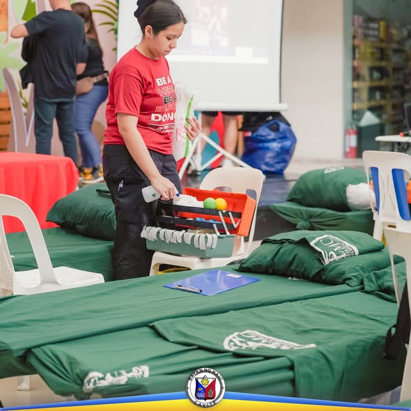 Mga kawani ng bloodletting activity na naghahanda ng mga gamit sa tabi ng mga higaan sa loob ng hall