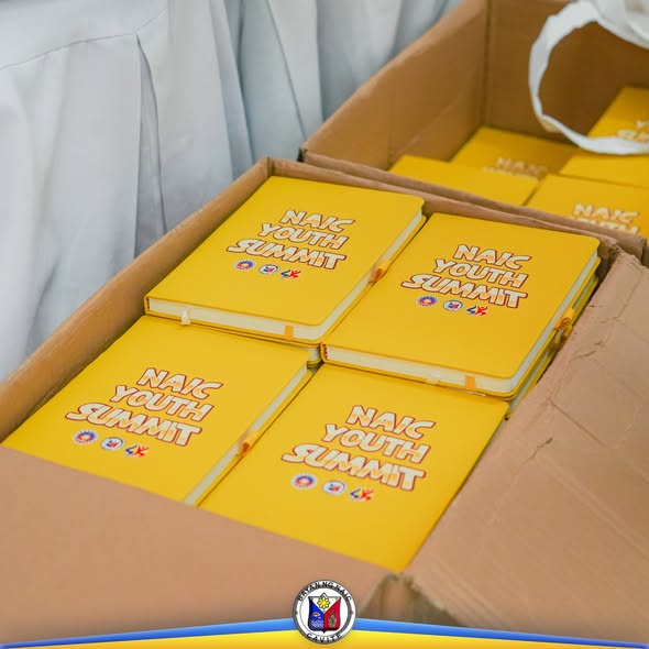 Mga yellow notebook na may print na "Naic Youth Summit" na nakaayos sa loob ng karton