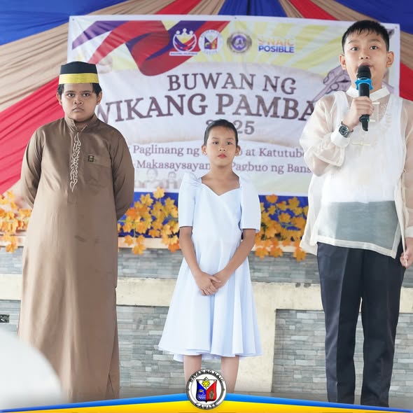 Tatlong bata sa entablado habang nagsasalita ang isa sa Buwan ng Wikang Pambansa 2025 sa Naic