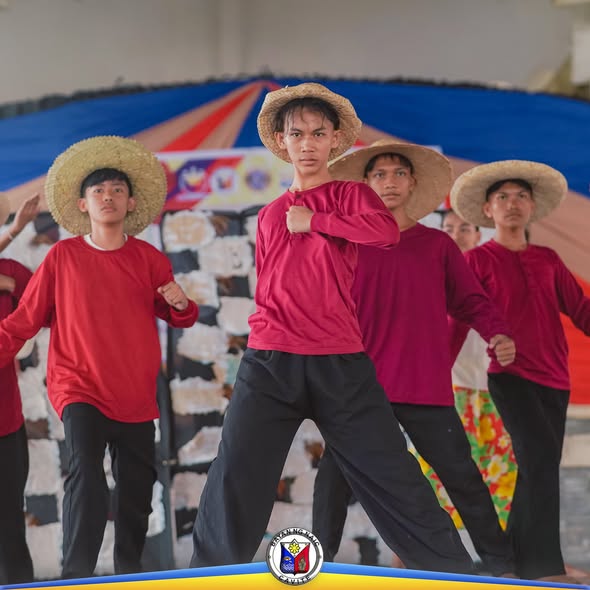 Mga mag-aaral na nagsasayw ng folk dance na naka-sombrero at pulang damit sa pagdiriwang ng Buwan ng Wikang Pambansa