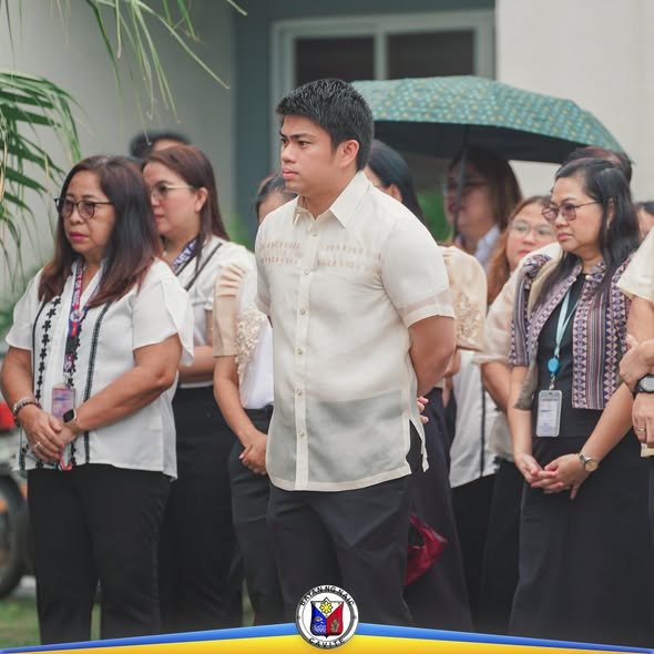 Mga kawani ng Pamahalaang Bayan ng Naic na nakatayo sa labas habang nasa Flag Raising Ceremony, may payong sa itaas.