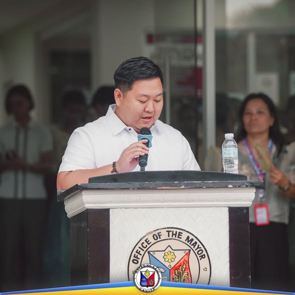 Lalaki na nagsasalita sa mikropono sa podium ng Office of the Mayor habang nasa flag raising ceremony ang mga kawani