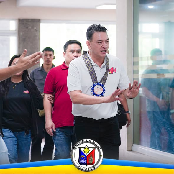 Mga opisyal na naglalakad sa pasilyo ng gusali, may logo ng Bayan ng Naic sa ibabang bahagi ng larawan.