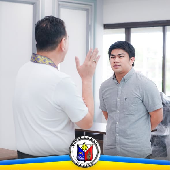 Dalawang opisyal na nag-uusap sa loob ng tanggapan sa Naic, may logo ng Bayan ng Naic
