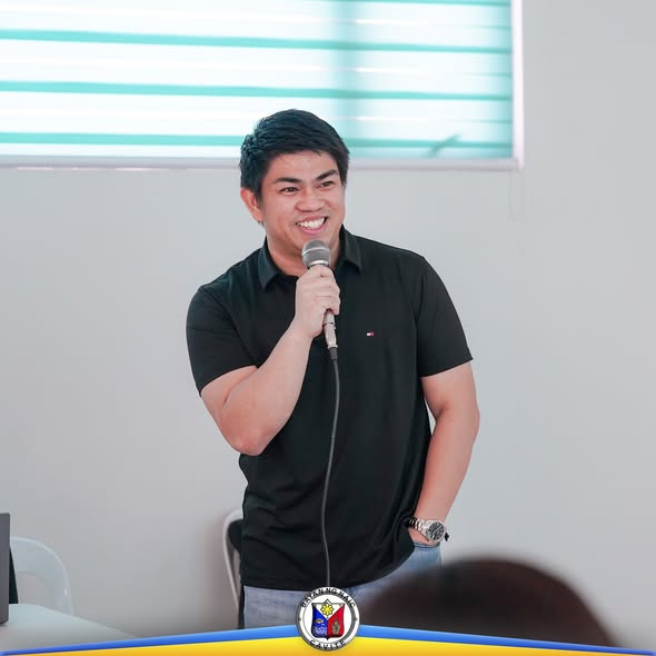 Lalaking naka-itim na polo na nagsasalita sa mikropono sa loob ng silid ng pagpupulong
