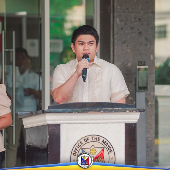 Lalaking nagsasalita sa mikropono sa podium ng Office of the Mayor sa flag raising ceremony sa Naic