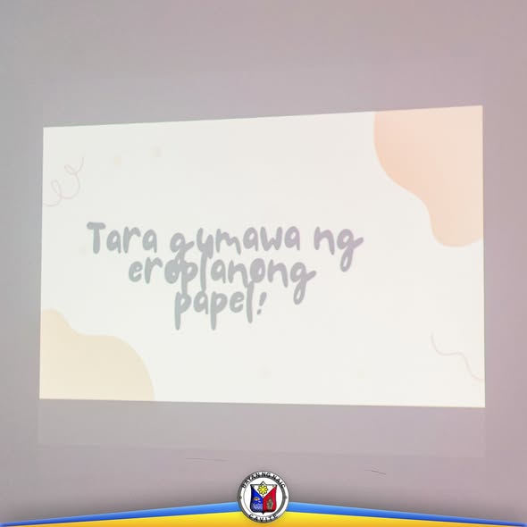 Slide: Tara gumawa ng eroplanong papel! Pastel na projection sa loob ng training hall.