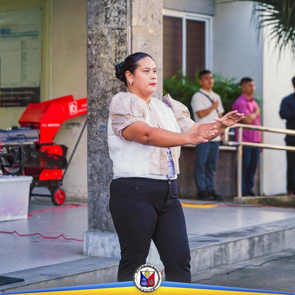Babaeng nagsasalita at nagpapaliwanag sa flag-raising ceremony ng Lokal na Pamahalaan ng Naic sa labas ng gusali