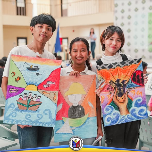 Tatlong kabataan na may hawak na makukulay na poster tungkol sa dagat at isda sa Fish Conservation Week, Naic