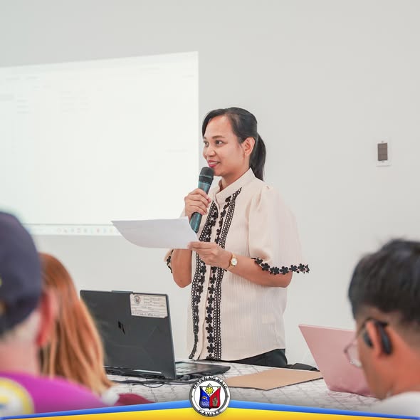 Babaeng nagsasalita sa mikropono sa Local Development Council Meeting sa Naic, may hawak na papel at laptop sa mesa