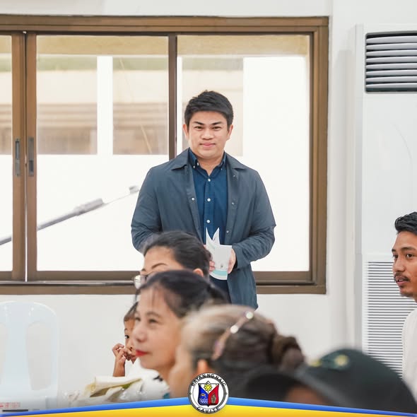 Lalaking nakatayo at may hawak na papel habang nakikinig ang mga dumalo sa Awarding of Checks sa Naic