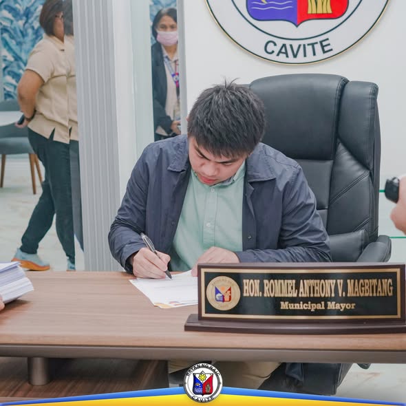 Isang opisyal na pumipirma ng dokumento sa mesa sa loob ng opisina ng Naic, Cavite