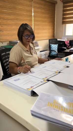 Isang babaeng pumipirma sa mga dokumento ng AIP sa opisina ng Naic
