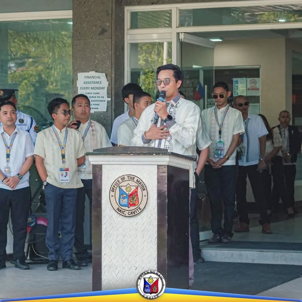 Nagsasalita ang isang opisyal sa podium ng Office of the Mayor, Naic habang nakikinig ang mga kawani sa labas ng munisipyo
