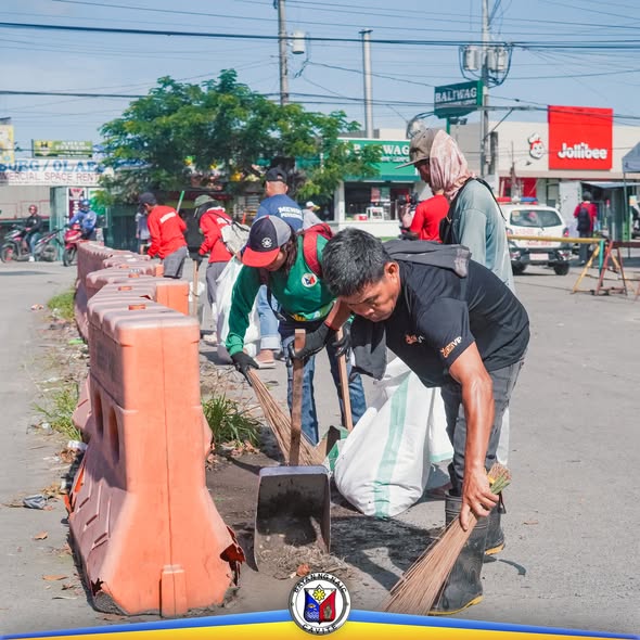 Mga tauhan na naglilinis ng kalsada sa Hills View, Naic, gamit ang walis at pala sa tabi ng mga harang