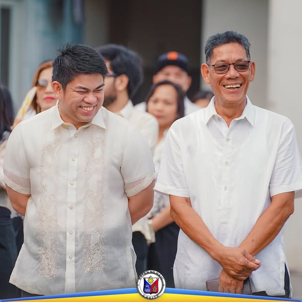 Dalawang nakangiting lalaki sa flag-raising ceremony ng OSCA sa Naic, nakasuot ng puting barong at polo