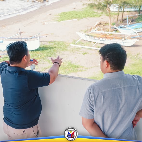 Dalawang lalaki na nakatingin at tumuturo sa dalampasigan kung saan nakahanay ang mga bangka sa Bucana Malaki