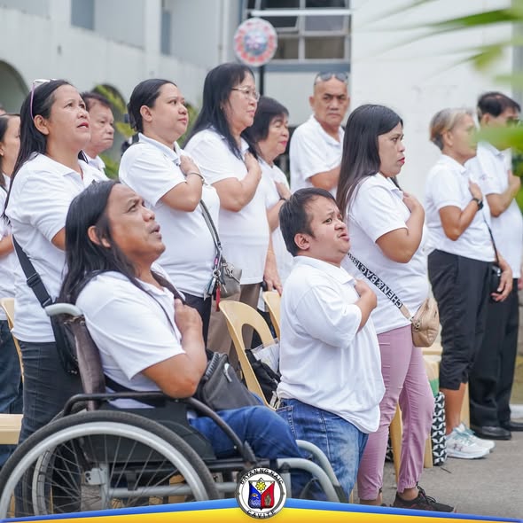 Mga kawani ng gobyerno na nakatayo at nakahawak sa dibdib habang nagpupugay sa watawat sa Naic Municipal Hall