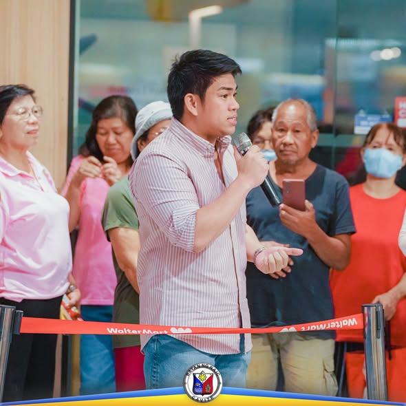 Lalaking nagsasalita sa mikropono sa harap ng mga senior citizen sa WalterMart, Brgy. Sabang, Naic
