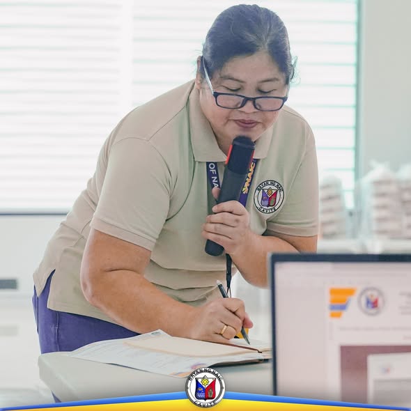 Babaeng opisyal na may hawak na mikropono habang nagsusulat sa notepad sa harap ng laptop, sa loob ng pulong